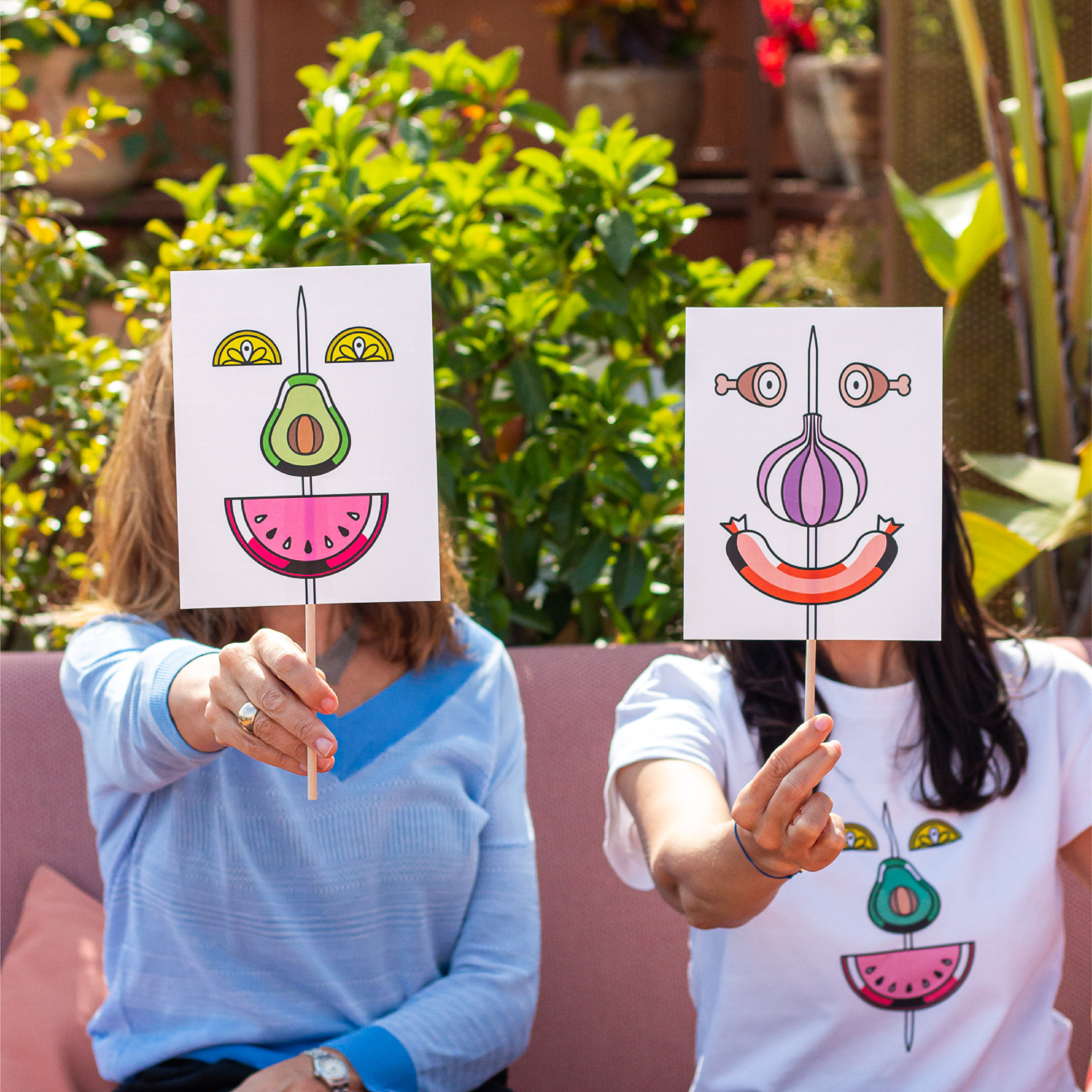 <span><span>Two women each holding a face mask infront of her face. The masks contain the graphics of the HOTEL TAPA TOUR 2023, where different elements of tapas appear forming a smiling face. Designed by the branding and communication studio/agency Esiete</span></span>