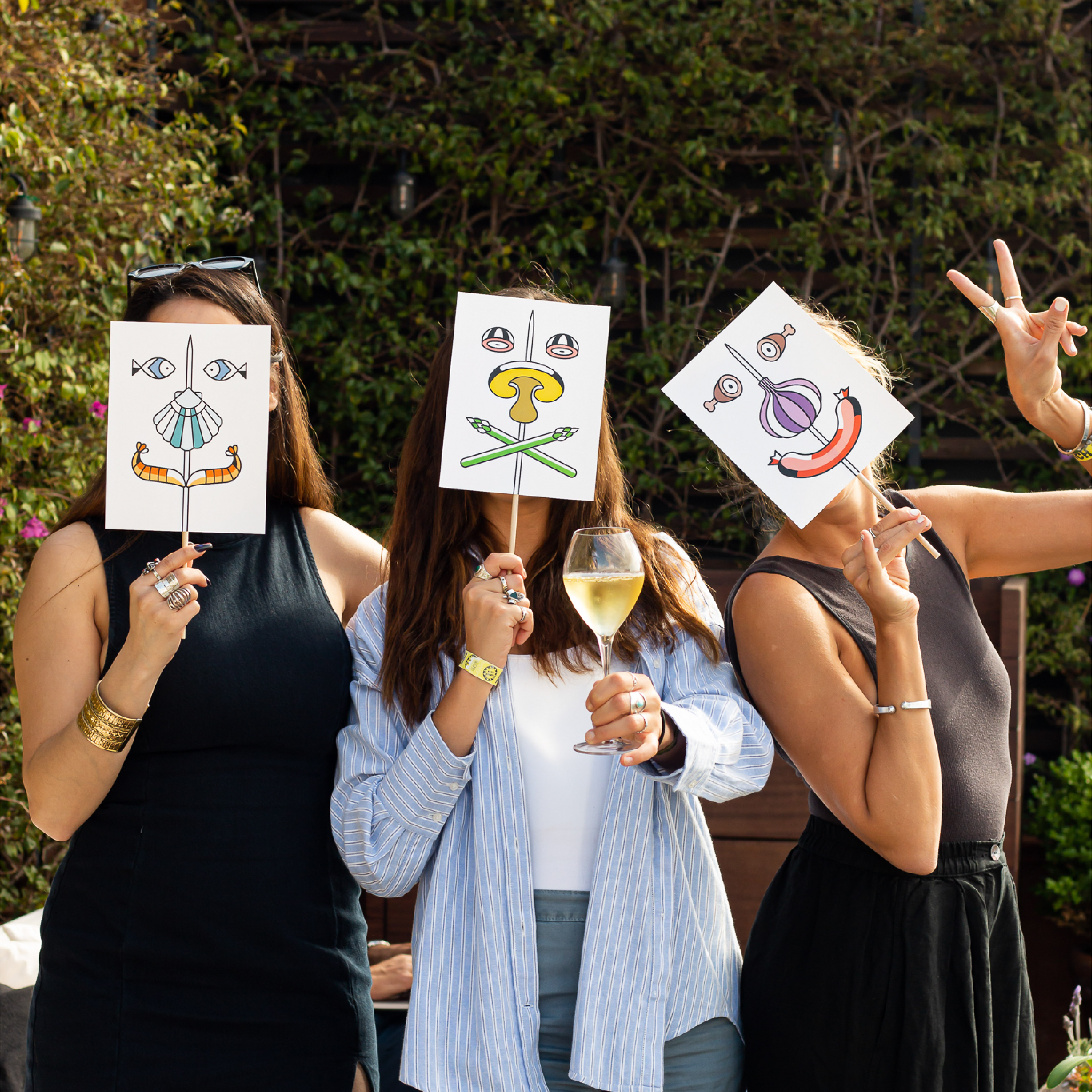 <span><span>Three women each holding a face mask infront of her face. The masks contain the graphics of the HOTEL TAPA TOUR 2023, where different elements of tapas appear forming a smiling face. Designed by the branding and communication studio/agency Esiete</span></span>