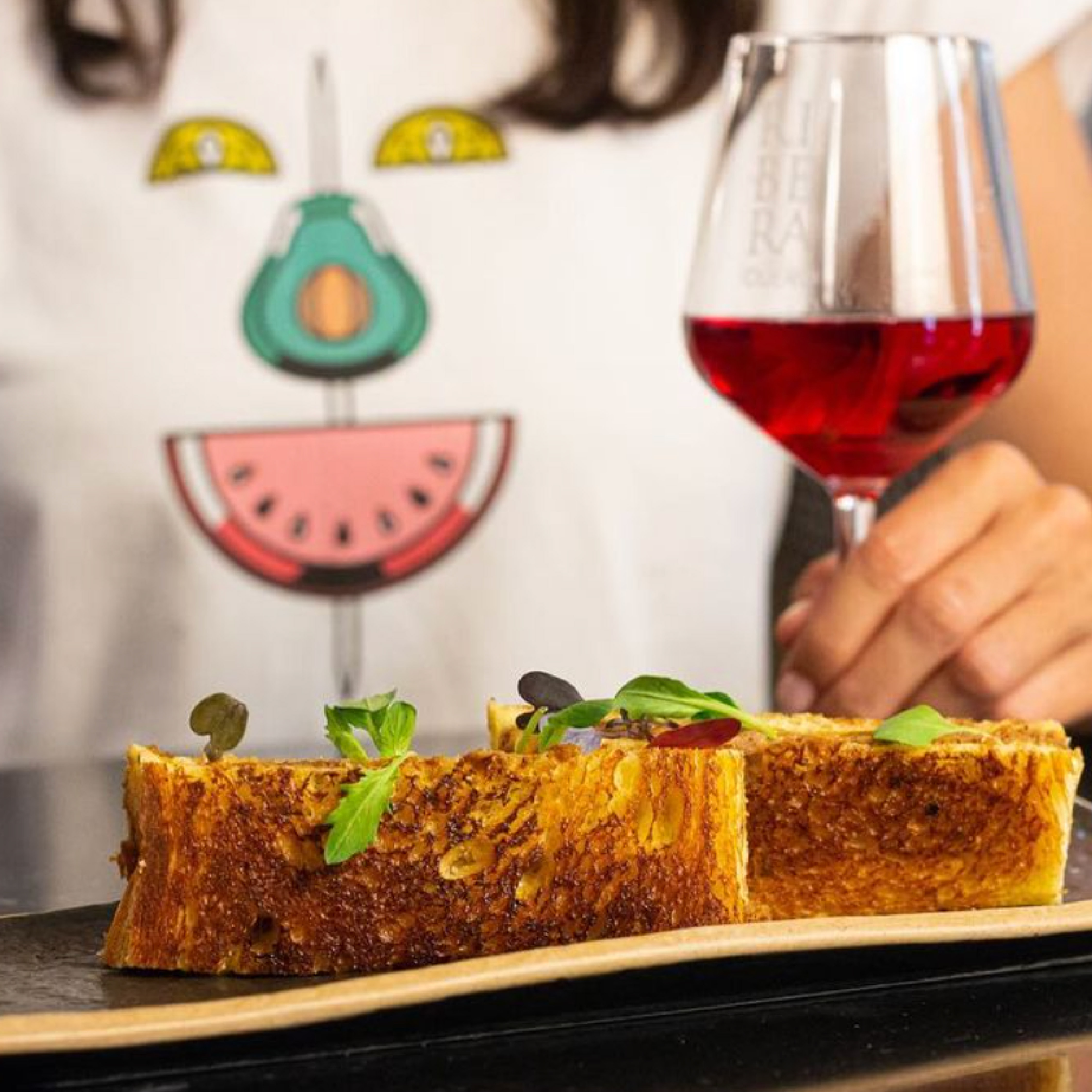 <span><span>A girl drinking wine and a toast of bread. She wears&nbsp; a t-shirt with the element of the graphic of HOTEL TAPA TOUR 2023. Designed by the branding and communication studio.</span></span>