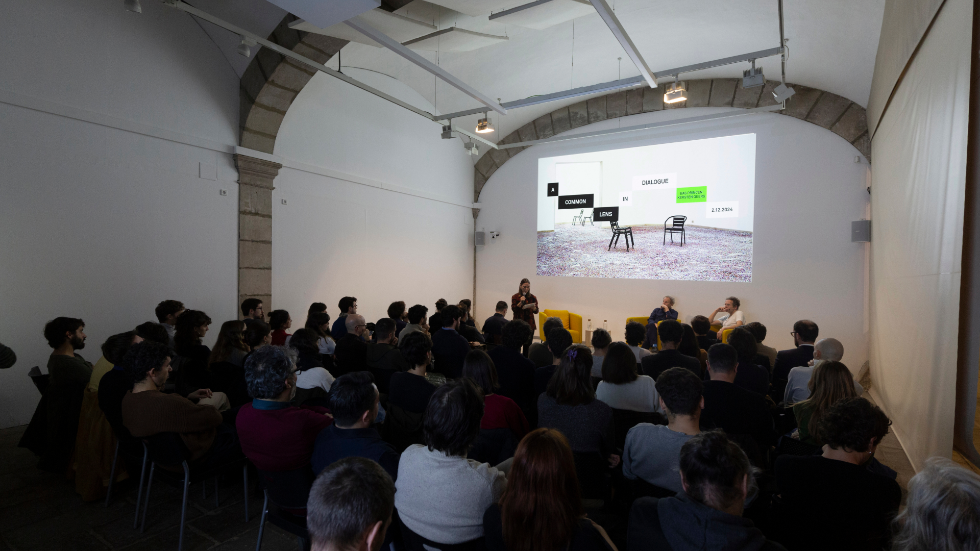 Exposici&oacute;n de la campa&ntilde;a de La Imagen Construida en La Virreina Centre de la Imatge, donde se muestran proyectadas las piezas gr&aacute;ficas en digital, mientras una multitud de gente observa la campa&ntilde;a gr&aacute;fica realizada por Esiete Studio, en un sistema reticular que genera composiciones din&aacute;micas, donde palabras e im&aacute;genes se construyen y deconstruyen en cuadrados negros y verdes.