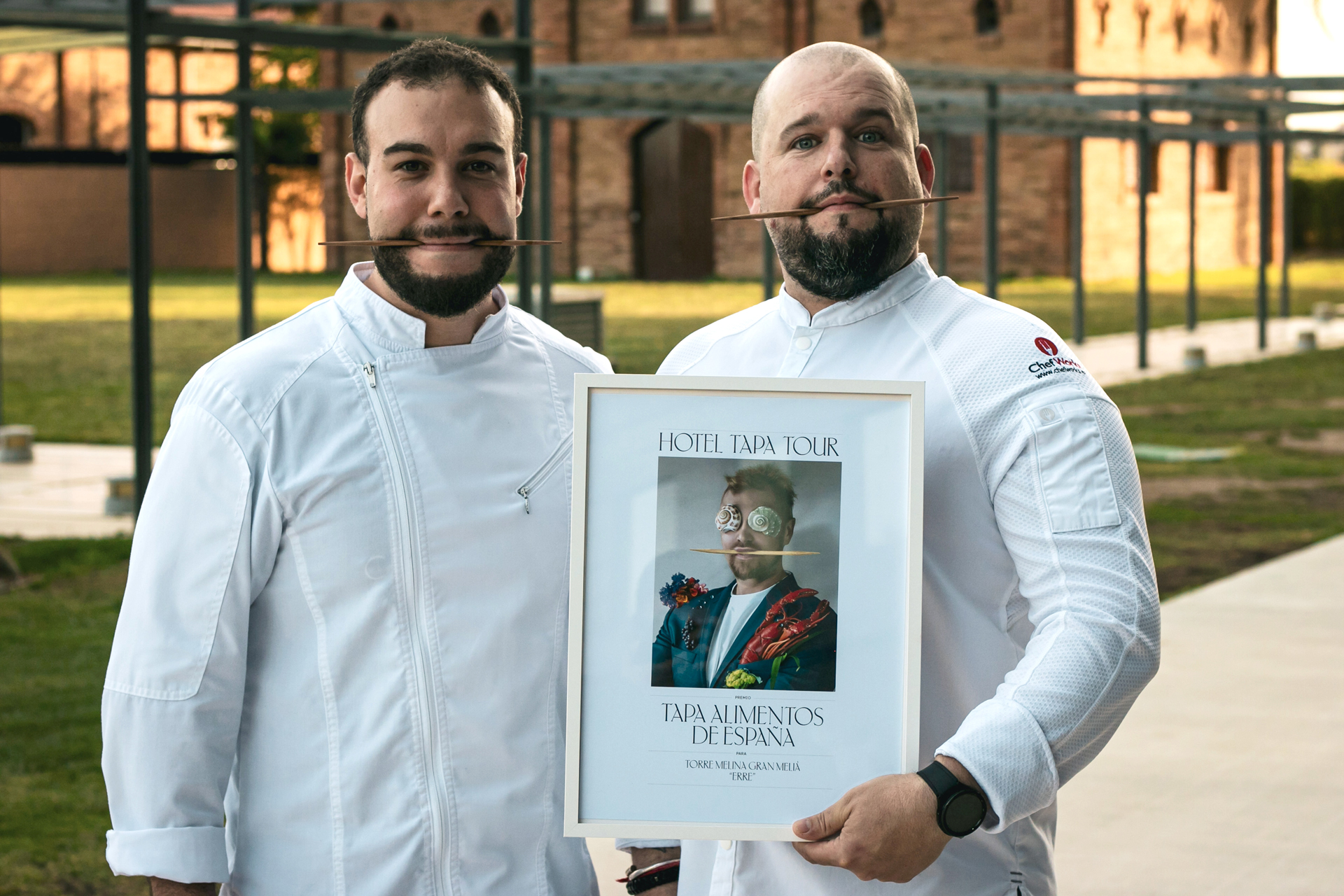 Dos chefs aparecen con un palillo en la boca y uno de ellos sujetando el premio de Hotel Tapa Tour de Tapas de alimentos de Espa&ntilde;a para Torre Melina Gran Meli&agrave; &ldquo;Erre&rdquo; escrito con una tipograf&iacute;a serif moderna y contempor&aacute;nea que forma parte de la identidad de Hotel Tapa Tour de 2024 junto a una imagen central de un chico con un traje azul oscuro lleno de ingredientes que se integran en su vestuario creando un collage surrealista, consiguiendo una aut&eacute;ntica pieza de moda culinaria que forma parte de la misma campa&ntilde;a desarrollada por el estudio de dise&ntilde;o gr&aacute;fico Esiete.